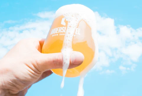 Hazy NEIPA in branded glass with thick foam and citrus aroma