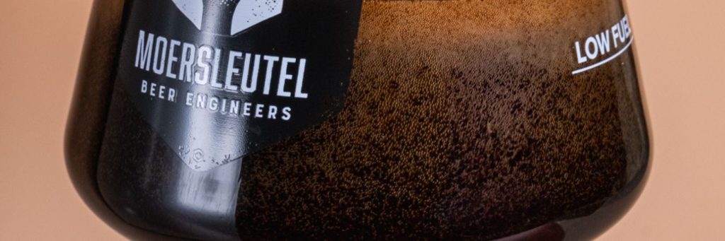 Een dik, donker speciaalbier (stout) uit het Moersleutel bierpakket Guild Dark, geserveerd in een glas op een houten tafel