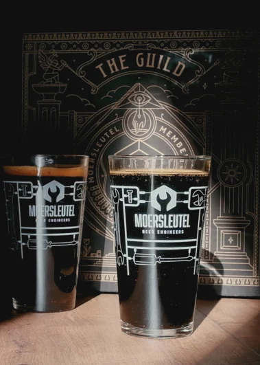 Moersleutel Vaasje glasses filled with dark beer, placed in front of a Moersleutel The Guild box