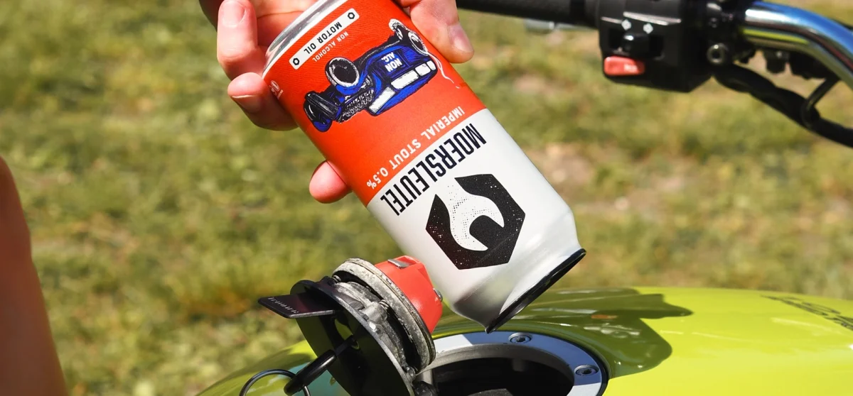Person playfully pouring Moersleutel Motor Oil Non-Alcoholic Stout into a motorcycle fuel tank